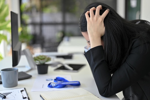 Side view of a stressed Asian businesswoman sits at her desk serious decision deadline frustrated