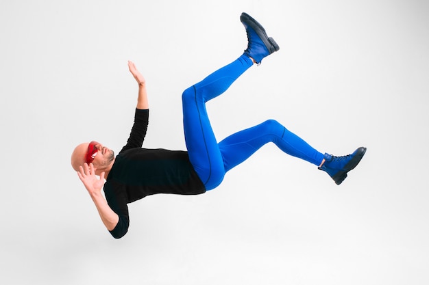 Side view of stylish man in futuristic red glasses and blue tights lying in air