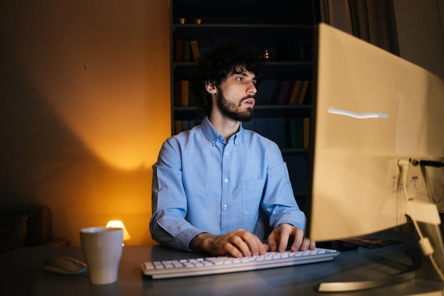 Side view of tired young business man working on computer in dark home office at night