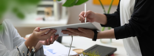 Side view of two businesswoman consulting on their project with digital tablet and office supplies