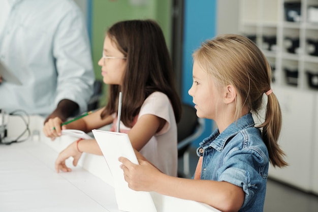 Side view of two youthful creative schoolgirls with documents and pencils