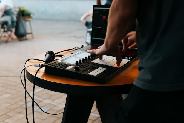 Side view of unrecognizable street musician beatmaker playing hip hop beats on drum machine midi controller at open air festival selective focus