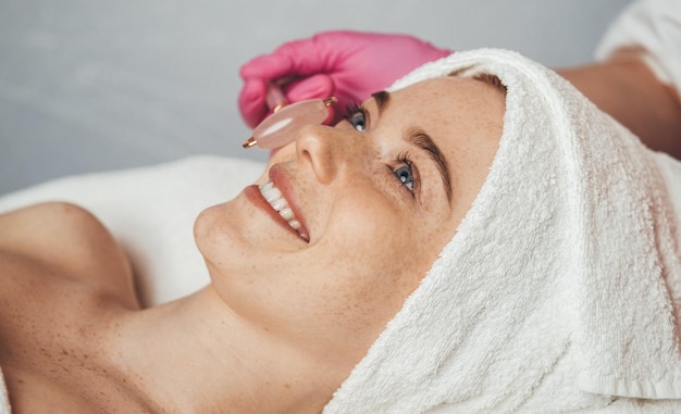 Side view of a woman lying on a massage bed receiving face massage in a beauty salon Fashionable modern Beauty spa treatment and relax concep