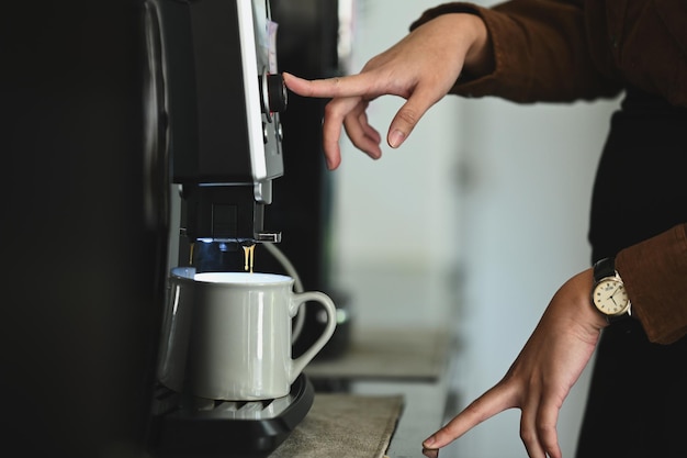 Side view of woman preparing fresh aromatic coffee using a coffee machine maker in cozy office kitchen