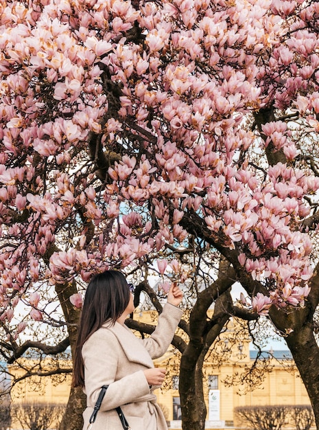 Side view of woman standing under beautiful pink magnolia tree in Zagreb, Croatia.