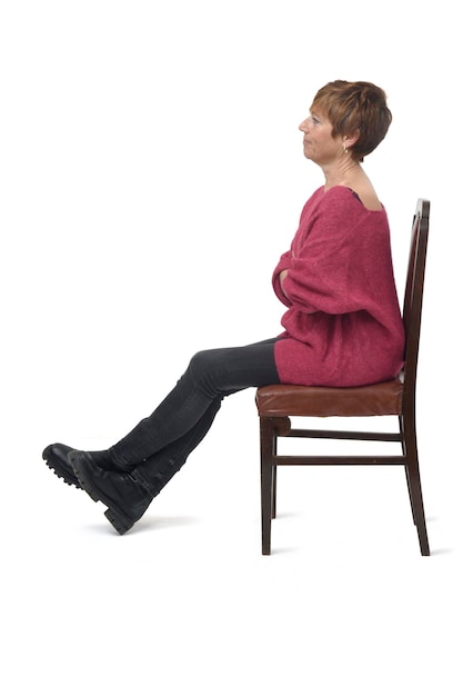 Side view of a woman in tight jean pants sitting on chair cross legged and arms crossed on white background