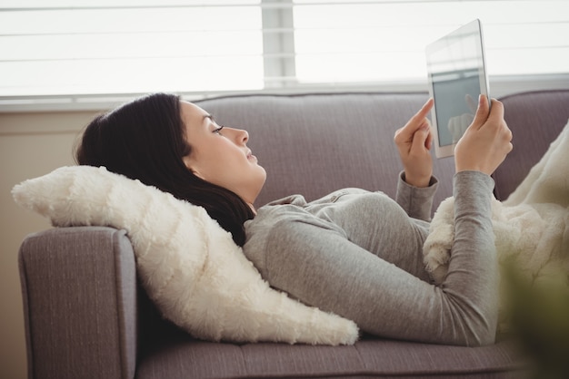 Side view of woman using tablet while lying on sofa