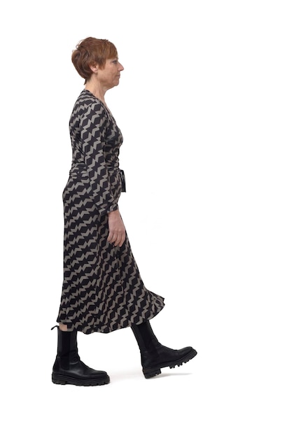 Side view of a woman with dress and boots walking and looking at camera on white background