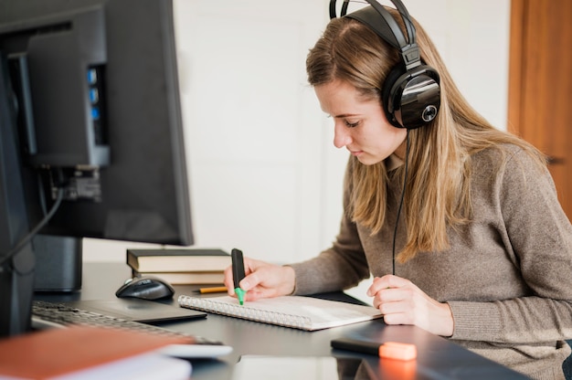 Side view of woman with headphones at desk participating in online class