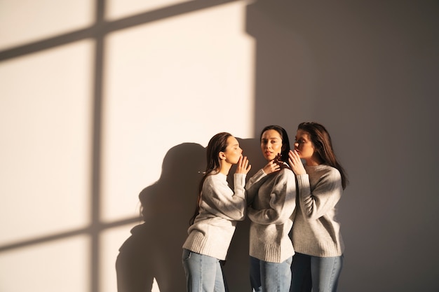 Side view of women in sweaters and jeans whispering to each other in window shadow