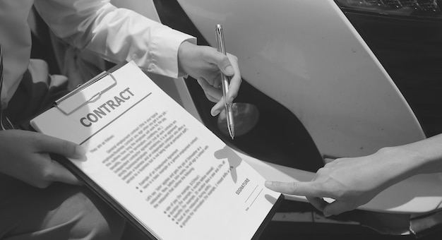 Photo side view of writing on clipboard while insurance agent examining car after accident