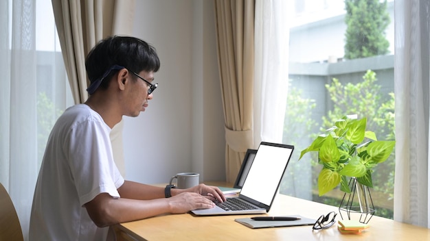 Side view young asian man sitting in comfortable living room and surfing internet on laptop computer