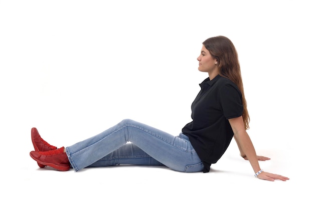 side view of a young girl sitting on the floor with straight legs on white background