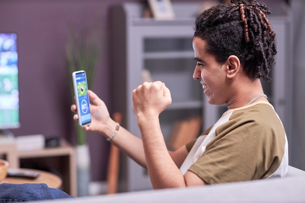 Side view young man winning online bet while watching sports match at home