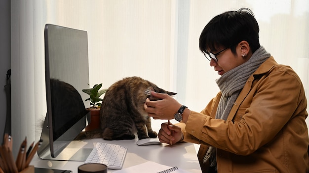 Side view of young man working from home and playing with his cute cat.