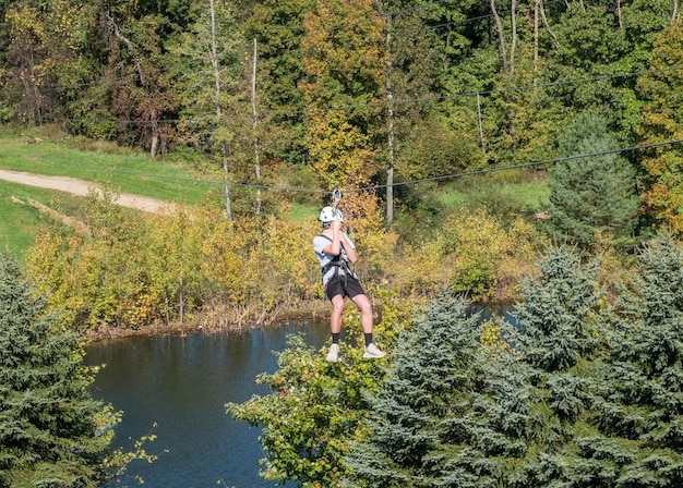 Side view of young man on zip line harness riding the zipline down between trees