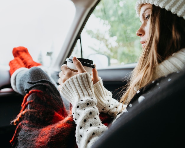 Sideways woman sitting in a car with a cup of coffee