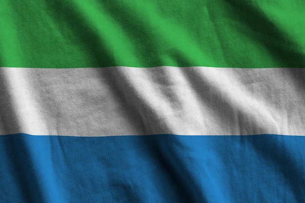 Sierra Leone flag with big folds waving close up under the studio light indoors The official symbols and colors in banner