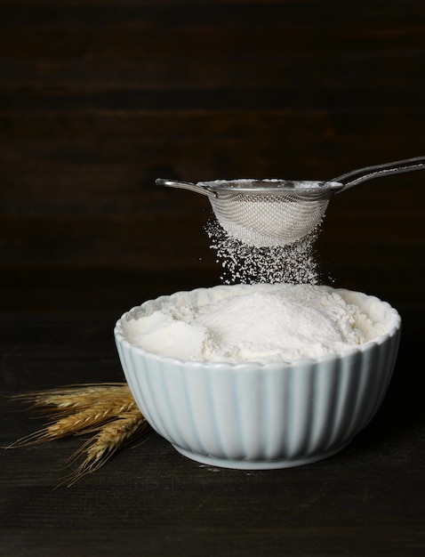 Sifting flour into bowl on table on wooden background