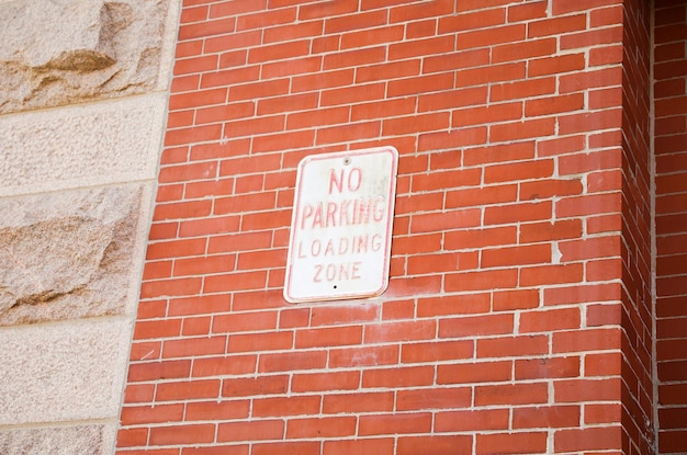 A sign on a brick wall that says no parking loading zone.