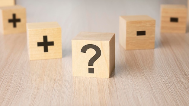 Sign question mark plus minus sign on the faces of a wooden cube mini wood cubes on wooden background