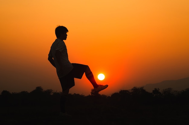 Silhouette action sport outdoors of a young man having fun playing soccer football for exercise under the sunset.