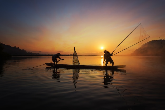 Silhouette of Asian fisherman on wooden boat