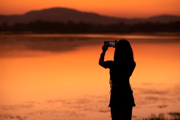 Silhouette Asian girl taking a photo by her mobile at tourist attractions in sunset,Sakonnakhon,Thailand.