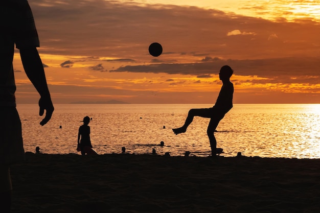 Silhouette of an Asian male player with a ball playing traditional beach football on beach by the sea at sunrise