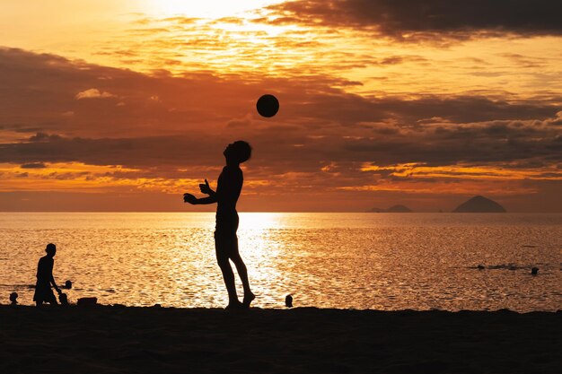 Silhouette of an Asian male player with a ball playing traditional sepak takraw football on beach by the sea at sunset