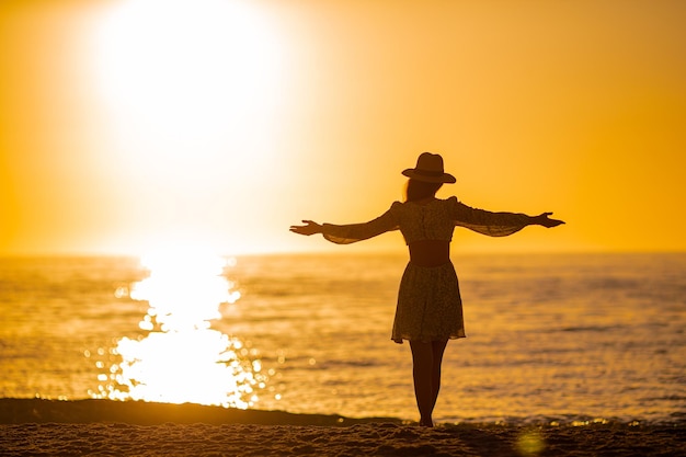 Silhouette of the beautiful woman in straw hat enjoying beautiful sunset on the beach