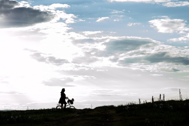 Silhouette beautiful young girl on bicycle a basket of blooming lilac in the countryside against a dramatic sky . Model plus size. Spring, rustic style