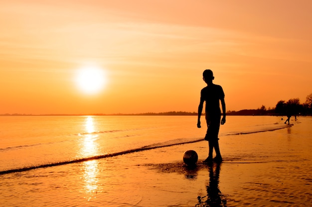 Silhouette of boy playing football on the beach