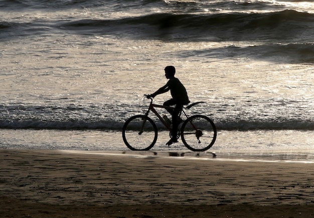 Silhouette of a boy riding a bike along the ocean after sunset