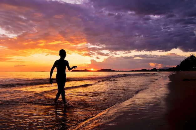 Silhouette of boy walking on the beach at sunset