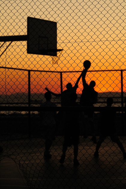 Silhouette of boys shooting hoops in the street.