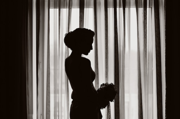 Silhouette of a bride with wedding bouquet at the window