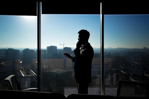 Silhouette of a businessman man in a modern office on the background of the window a man talking on the phone