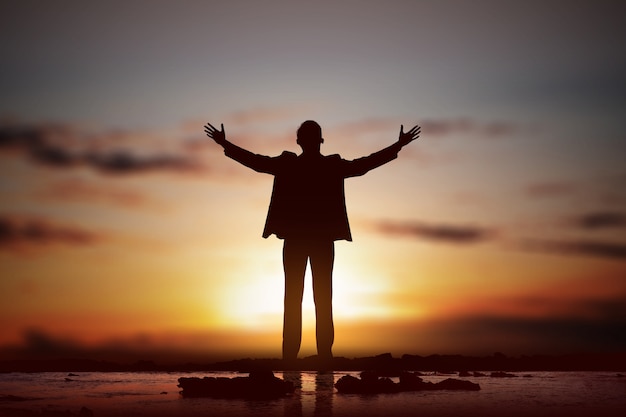 Silhouette of businessman raised hands and praying to god 