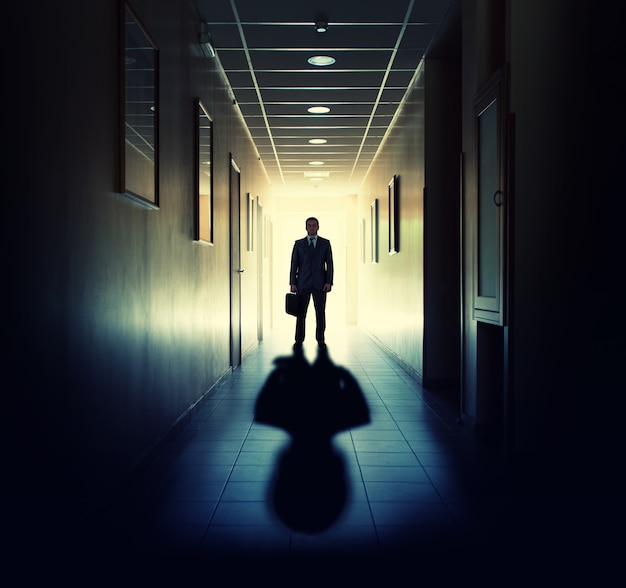 Silhouette of businessman standing in office building corridor against light