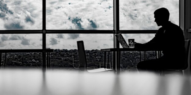 Silhouette of a businessman working in an office with large windows.