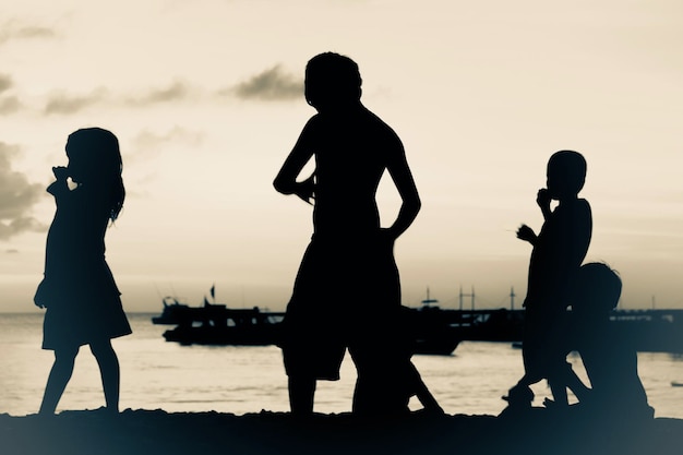 Silhouette children at beach against sky during sunset