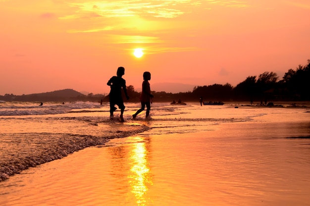 silhouette of children walking on the beach at sunset