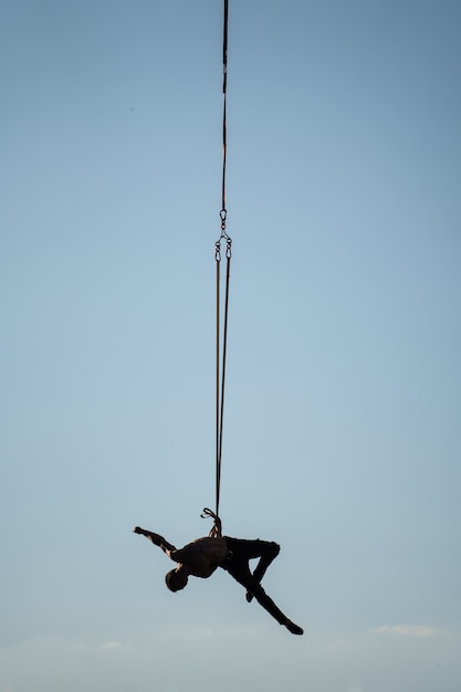 Silhouette of circus artist on the aerial straps on blue sky background