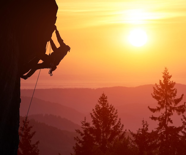 Silhouette of climber hanging on cliff Landscape of mountain peaks sunshine on background Over filtered copy space