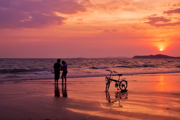 Silhouette of couple standing on the beach with dramatic sunset sky