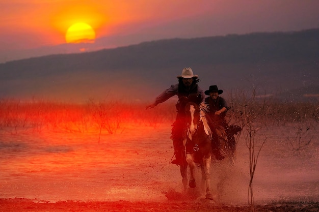 Silhouette of a cowboy riding a horse wading through the water at sunset behind a mountain