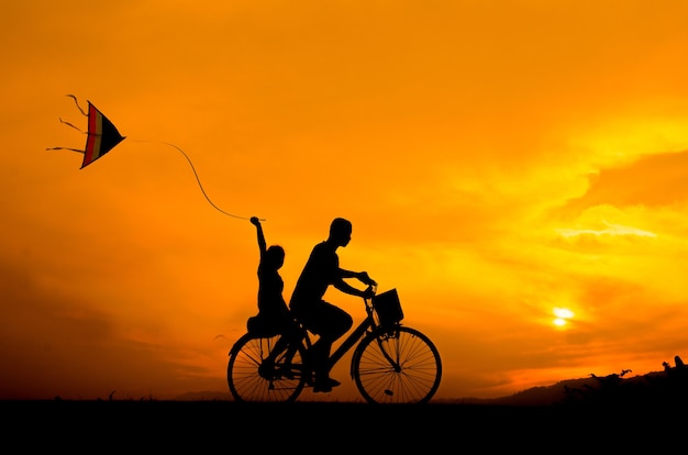 silhouette cycling brother and sister with kite.