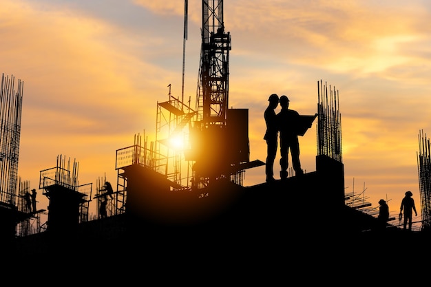 Silhouette of Engineer and worker team on building site, construction site with sunset in evening time