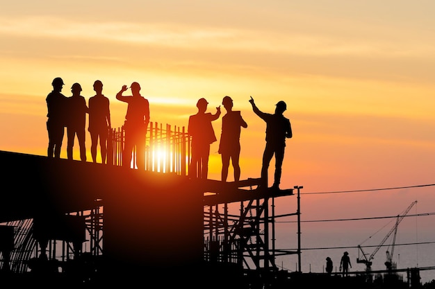 Silhouette of Engineer and worker team on building site, Industrial sector construction site at sunset in evening time